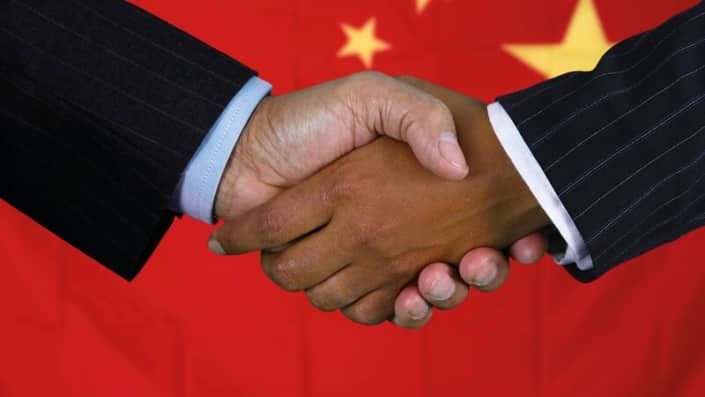 Close-up van een handshake tussen een zwarte en een Chinese persoon met de Chinese vlag op de achtergrond