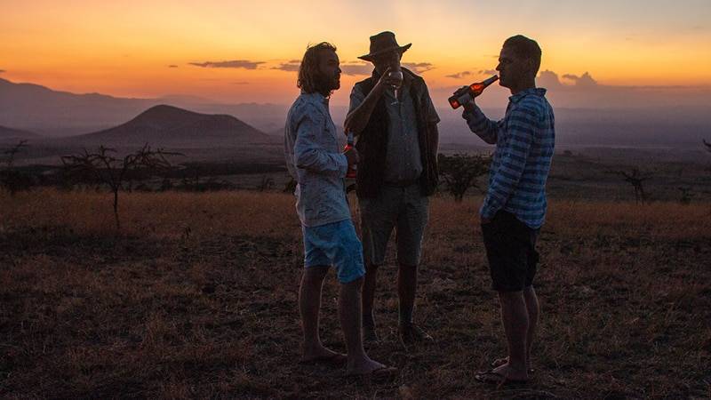 Charlie en 2 andere personen staan in een veld en drinken wat bij een zonsondergang